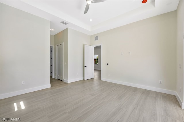 unfurnished room featuring ceiling fan, a tray ceiling, and light hardwood / wood-style floors