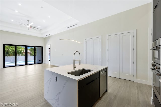 kitchen with sink, light hardwood / wood-style flooring, dishwasher, an island with sink, and decorative light fixtures