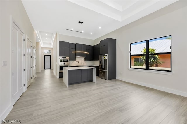 kitchen featuring wall chimney exhaust hood, sink, light hardwood / wood-style flooring, a kitchen island, and stainless steel appliances