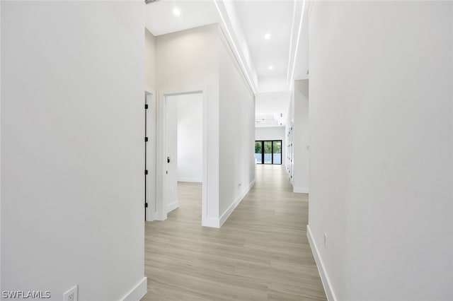 hall featuring a towering ceiling and light wood-type flooring