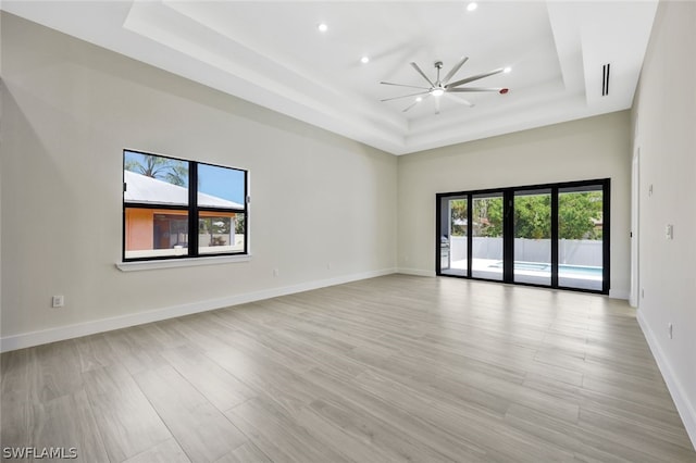 spare room with a raised ceiling, ceiling fan, a high ceiling, and light hardwood / wood-style floors