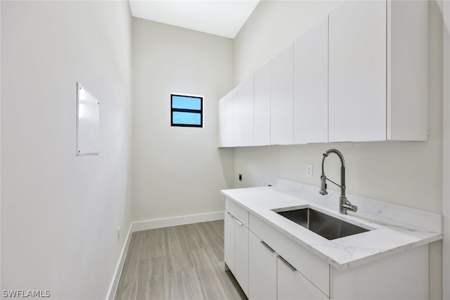 kitchen featuring sink, light stone countertops, white cabinets, and light wood-type flooring