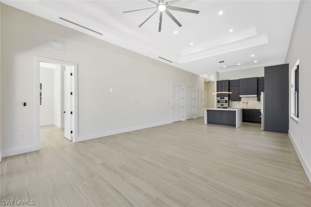 unfurnished living room with ceiling fan, a raised ceiling, and light wood-type flooring