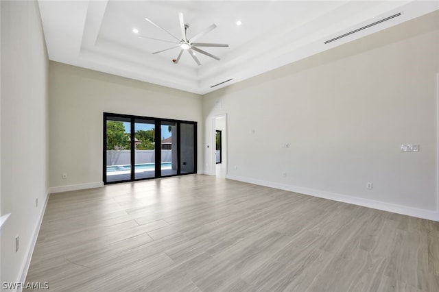 spare room featuring a raised ceiling, a towering ceiling, ceiling fan, and light hardwood / wood-style flooring