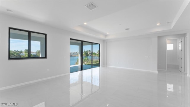 unfurnished room featuring a water view, a wealth of natural light, and a tray ceiling