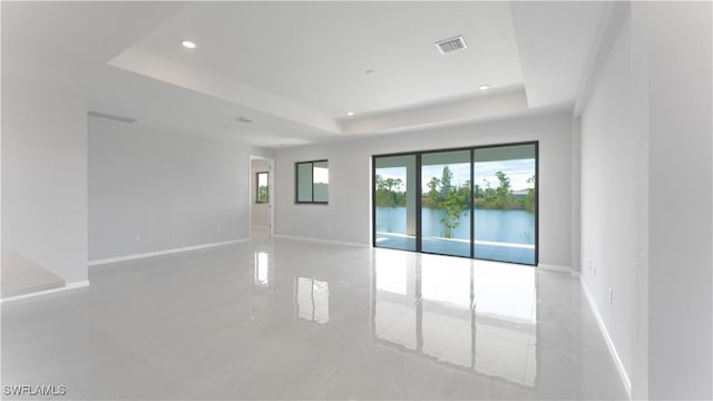 empty room with a raised ceiling, light tile patterned floors, and a water view