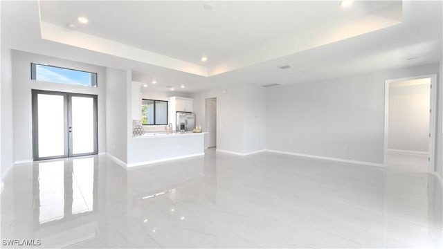 unfurnished living room featuring a raised ceiling, french doors, and sink