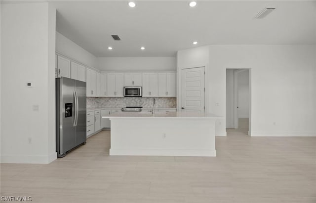 kitchen featuring appliances with stainless steel finishes, tasteful backsplash, white cabinetry, and an island with sink