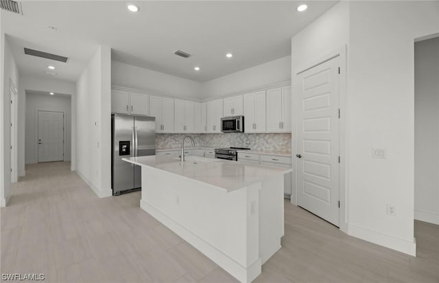 kitchen with sink, an island with sink, appliances with stainless steel finishes, tasteful backsplash, and white cabinetry