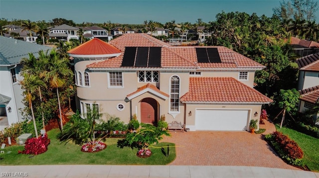 mediterranean / spanish house featuring solar panels, a garage, and a front yard