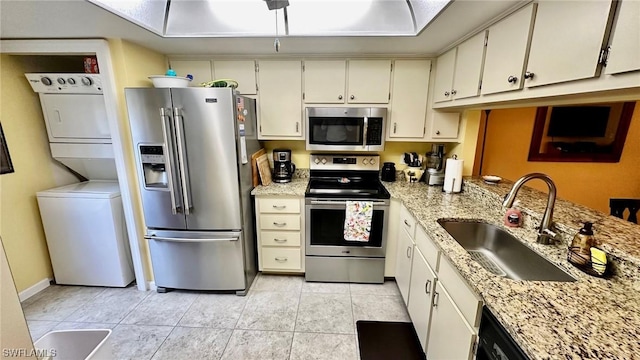 kitchen featuring sink, light stone countertops, appliances with stainless steel finishes, white cabinetry, and stacked washer / dryer