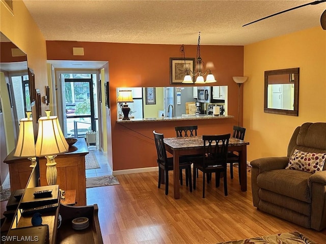 dining area with a textured ceiling, light hardwood / wood-style flooring, and an inviting chandelier