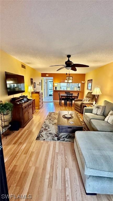 living room featuring a textured ceiling, light hardwood / wood-style flooring, and ceiling fan