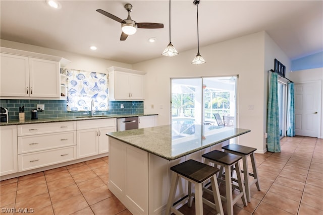 kitchen featuring ceiling fan, sink, a kitchen island, white cabinetry, and light stone countertops