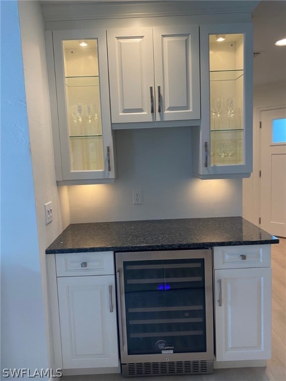 bar with white cabinets, light hardwood / wood-style flooring, wine cooler, and dark stone counters