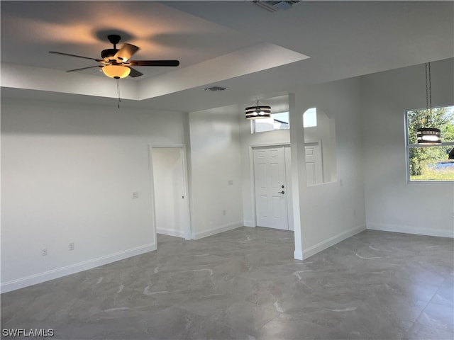 tiled empty room featuring a raised ceiling and ceiling fan