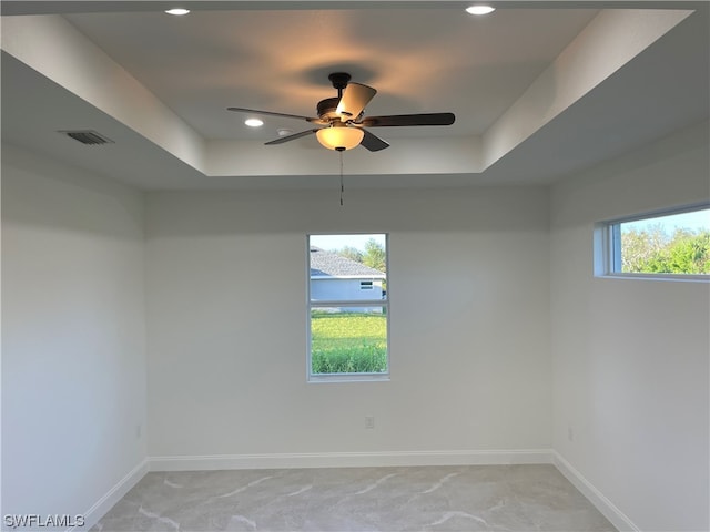 unfurnished room with a raised ceiling, ceiling fan, and a wealth of natural light