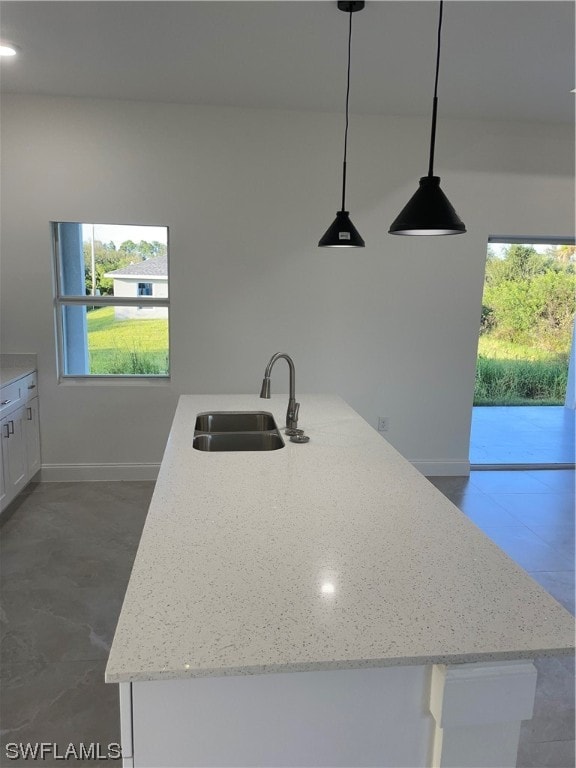 kitchen featuring light stone countertops, hanging light fixtures, white cabinetry, dark tile floors, and sink