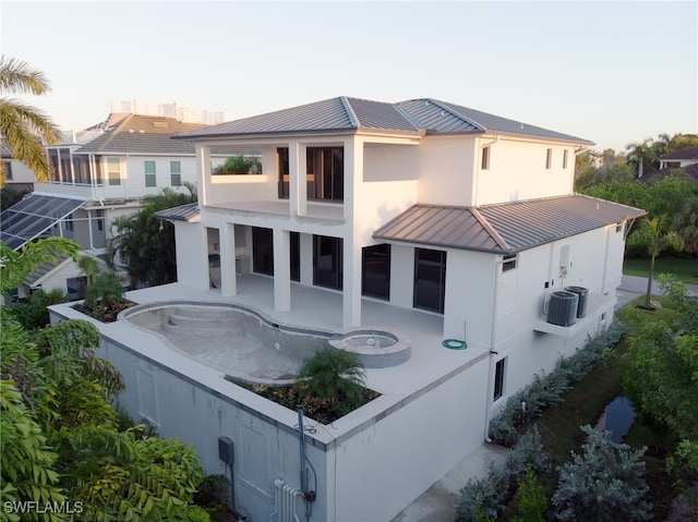 back house at dusk with a balcony, central AC unit, and a patio area