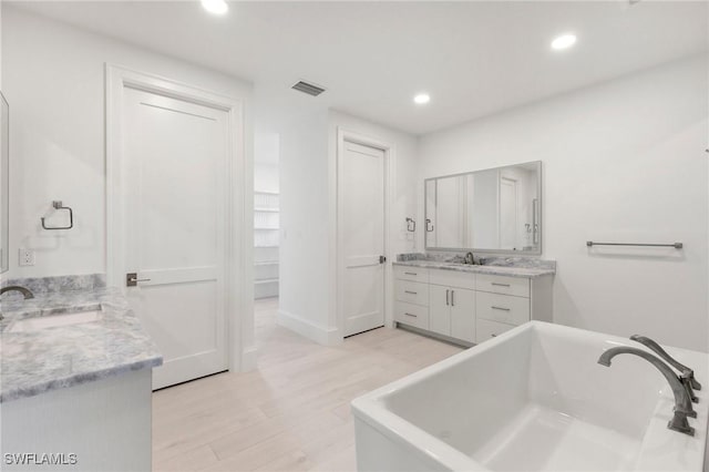 375 Periwinkle Ct, Marco Island, FL 34145 - bathroom featuring wood finished floors, a sink, two vanities, a soaking tub, and visible vents