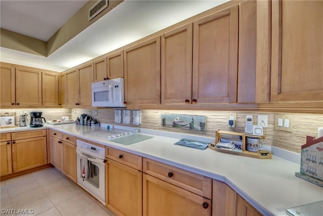 kitchen with light tile patterned floors, backsplash, and white appliances