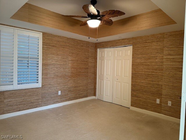 unfurnished bedroom featuring a raised ceiling, light colored carpet, a closet, and ceiling fan