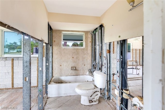 bathroom featuring a tub, tile flooring, toilet, and tile walls