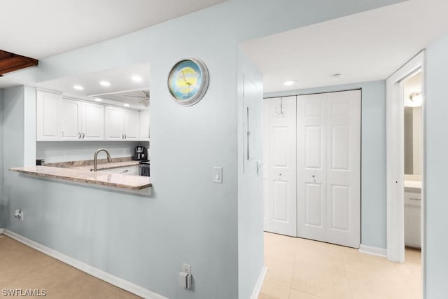 kitchen featuring sink, kitchen peninsula, light stone countertops, light tile patterned floors, and white cabinetry