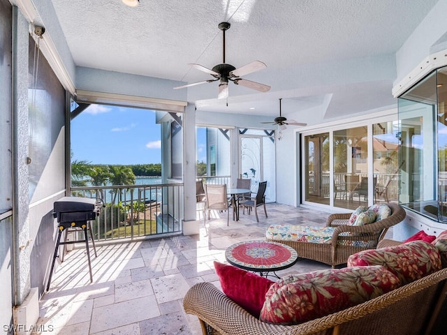 sunroom featuring ceiling fan and a water view