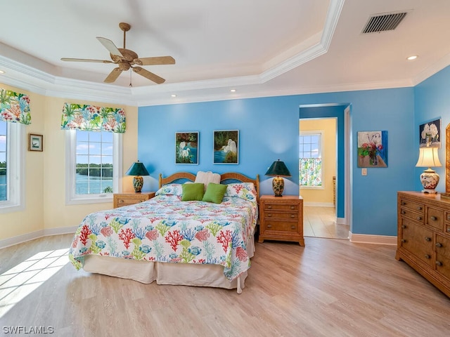 bedroom featuring ceiling fan, ornamental molding, light hardwood / wood-style flooring, and a tray ceiling