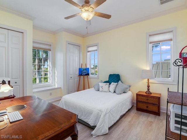 bedroom with ornamental molding, two closets, ceiling fan, and light hardwood / wood-style floors