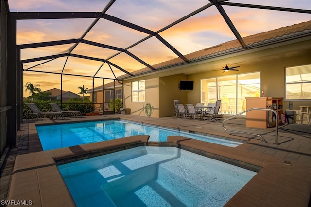 pool at dusk featuring an in ground hot tub, a patio area, ceiling fan, and a lanai