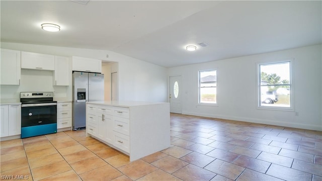 kitchen with appliances with stainless steel finishes, vaulted ceiling, light tile patterned floors, a kitchen island, and white cabinetry