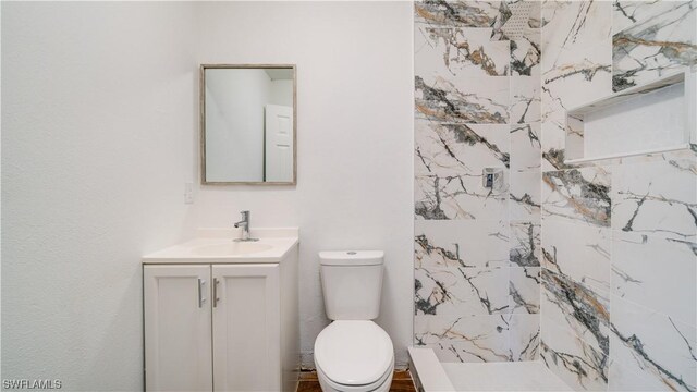 bathroom with tiled shower, toilet, and vanity