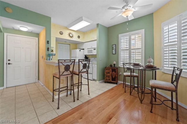 kitchen featuring white appliances, a kitchen breakfast bar, white cabinets, kitchen peninsula, and light wood-type flooring