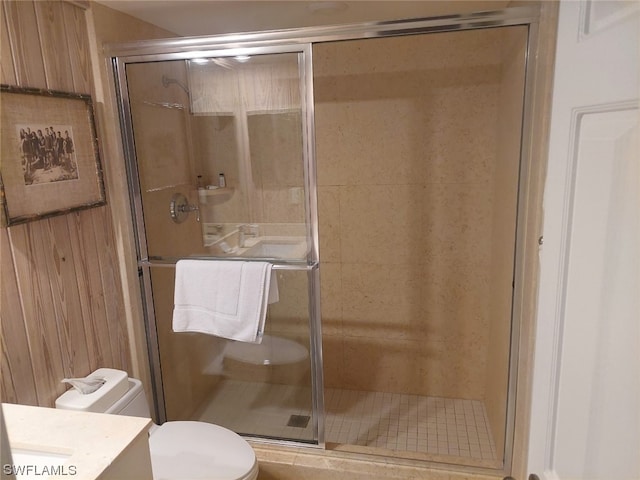 bathroom featuring a shower with door, vanity, wooden walls, and toilet