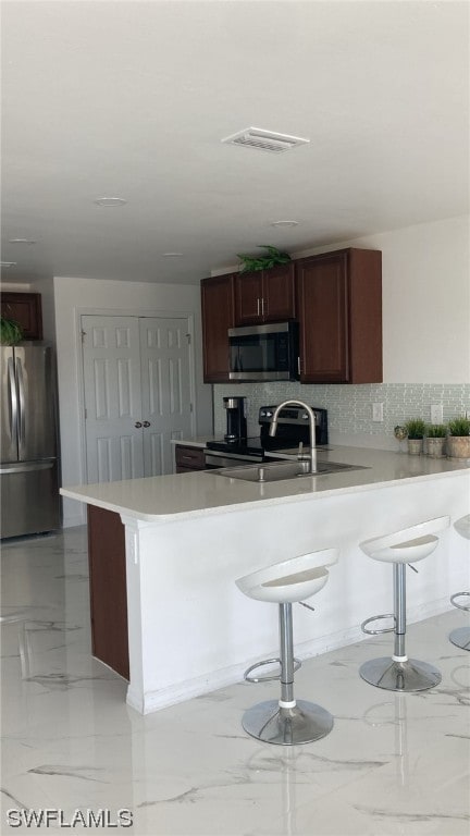 kitchen featuring sink, a breakfast bar area, kitchen peninsula, stainless steel appliances, and backsplash