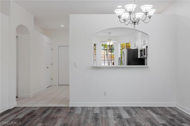 unfurnished dining area featuring ceiling fan with notable chandelier and light hardwood / wood-style flooring