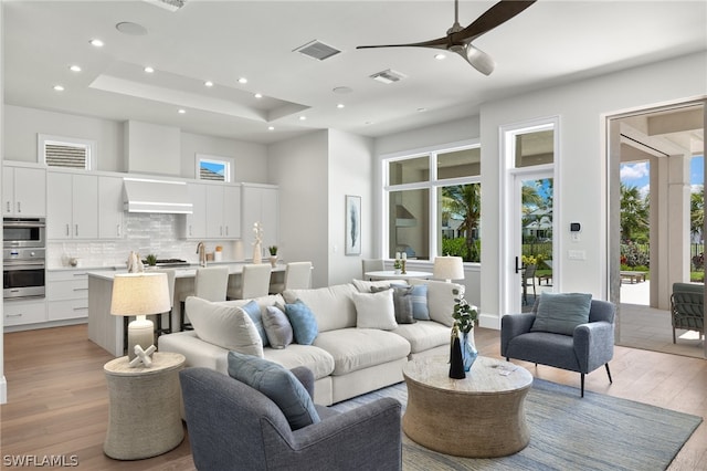 living room featuring ceiling fan, sink, light hardwood / wood-style floors, and a raised ceiling