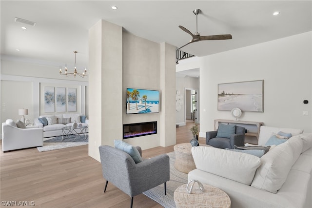 living room featuring a high ceiling, ceiling fan with notable chandelier, light hardwood / wood-style flooring, and a large fireplace