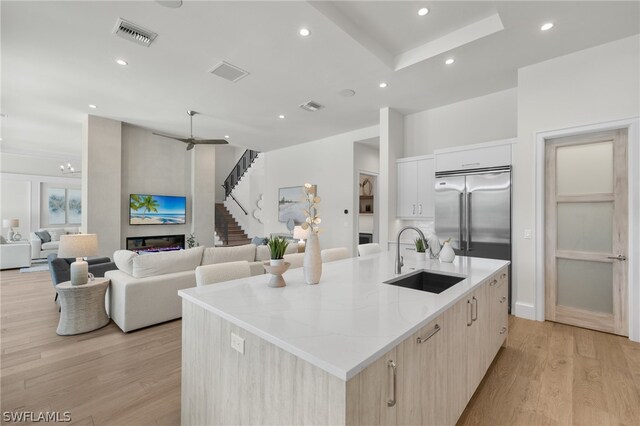 kitchen with light stone countertops, light hardwood / wood-style flooring, a kitchen island with sink, built in fridge, and sink