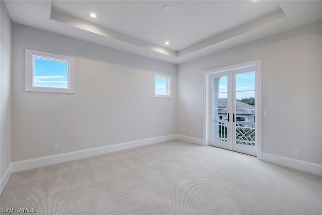 carpeted spare room featuring a tray ceiling and french doors