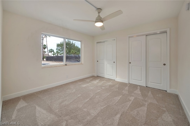 unfurnished bedroom featuring light colored carpet, two closets, and ceiling fan