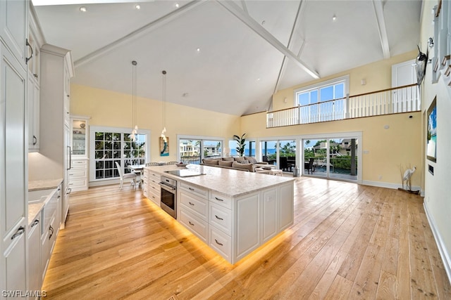 kitchen featuring white cabinetry, stainless steel oven, light hardwood / wood-style floors, a center island with sink, and high vaulted ceiling