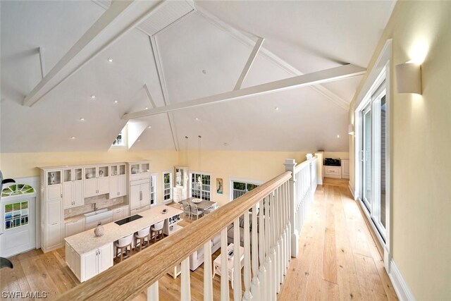 corridor featuring light wood-type flooring and vaulted ceiling with beams