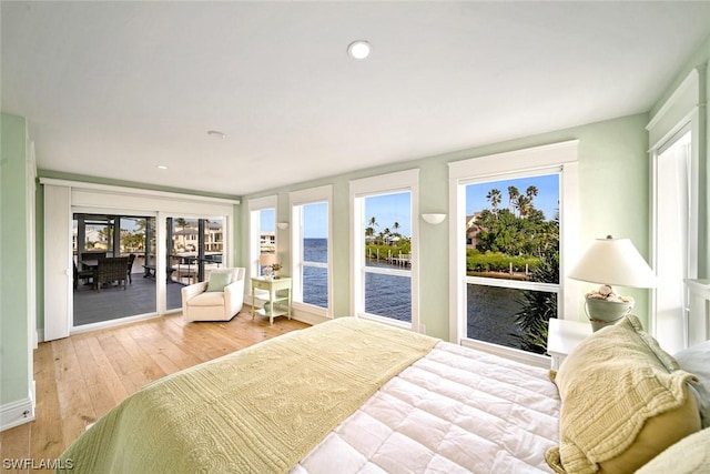 bedroom with access to exterior, light hardwood / wood-style flooring, and a water view