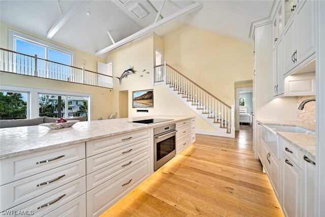 kitchen featuring white cabinets, sink, oven, and light wood-type flooring