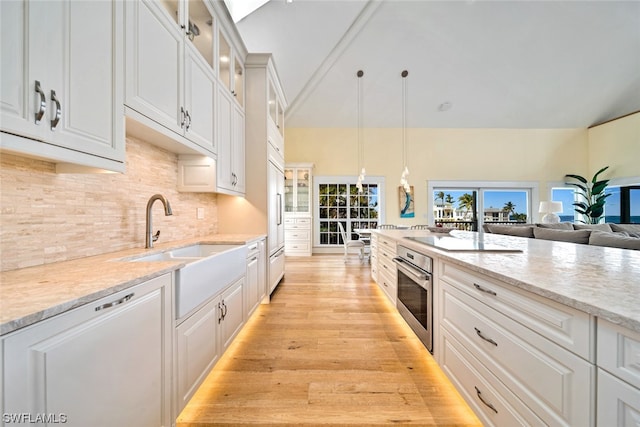 kitchen with hanging light fixtures, light hardwood / wood-style floors, decorative backsplash, stainless steel oven, and white cabinetry