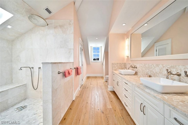 bathroom with hardwood / wood-style flooring, tiled shower, vanity, vaulted ceiling, and toilet