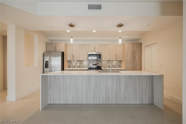 kitchen with tasteful backsplash, appliances with stainless steel finishes, pendant lighting, a large island with sink, and sink